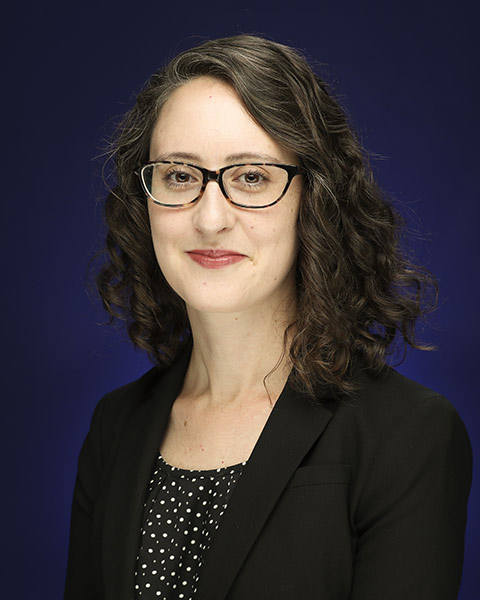 Alexandra Cavallaro smiles facing the camera against a dark backdrop