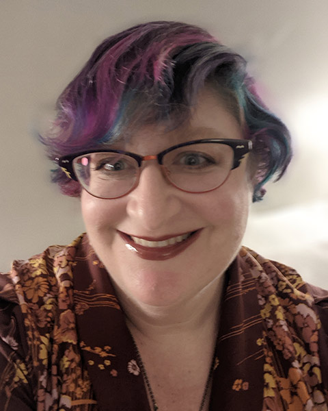 A headshot of Beth Bruch smiling, wearing a flowered shirt on a plain background