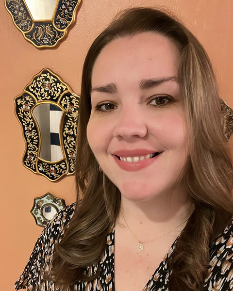 Laura Gonzalez PhD, a femme-presenting person with white skin and brown hair smiles and looks at the camera.