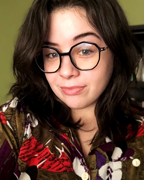 Jami Padgett, a white person with circular glasses, smiles against a yellow background