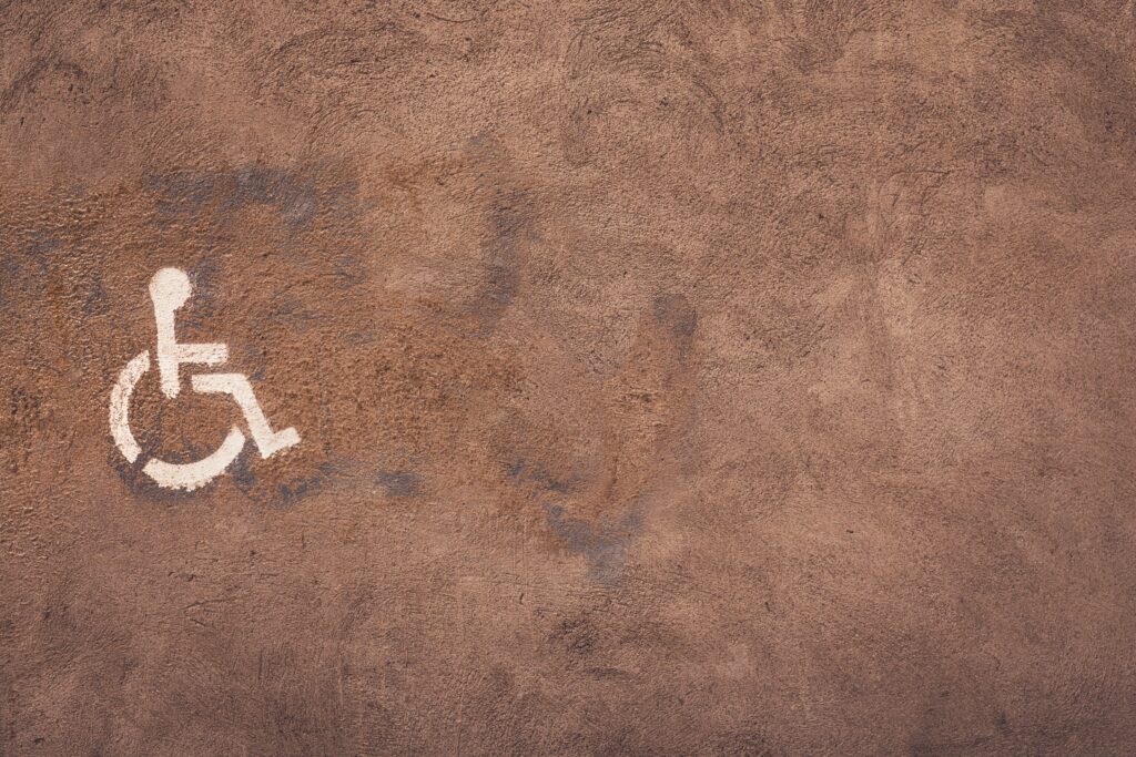 A disability symbol (person in wheel chair) spray painted in white upon a brown wall.